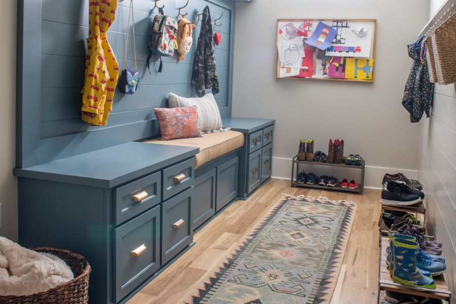 Custom blue built-in mudroom bench with storage hooks and family-friendly runner rug in a functional entryway