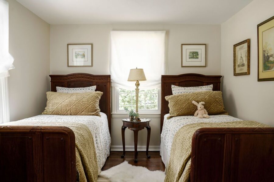 Small bedroom with twin beds and one central round nightstand holding a lamp, styled for symmetry and efficient use of space.