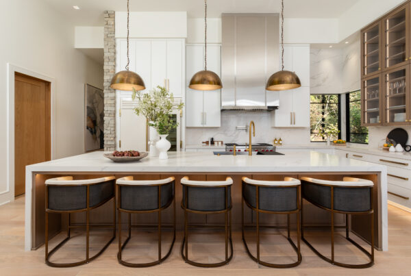 Modern kitchen with large brass pendant lights over an island, white cabinetry, and marble accents.