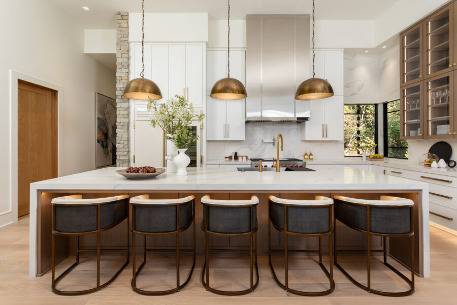 Modern kitchen with large brass pendant lights over an island, white cabinetry, and marble accents.