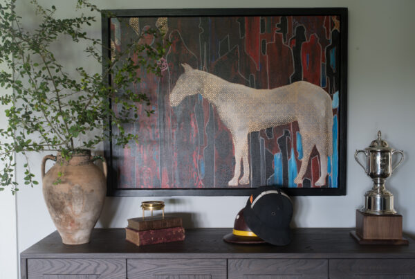 Console table styled with equestrian artwork, vintage trophies, a riding helmet, books, and an oversized urn with greenery.