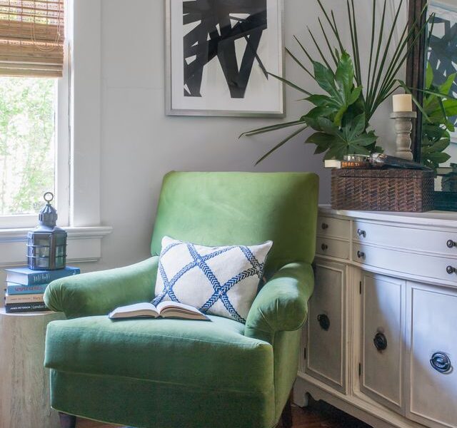 Cozy reading nook with a green velvet chair, abstract black-and-white art, and layered greenery styled by Nandina Home & Design.