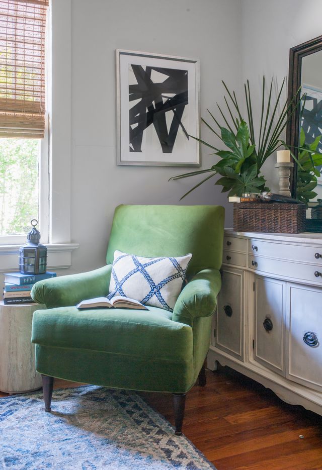 Cozy reading nook with a green velvet chair, abstract black-and-white art, and layered greenery styled by Nandina Home & Design.